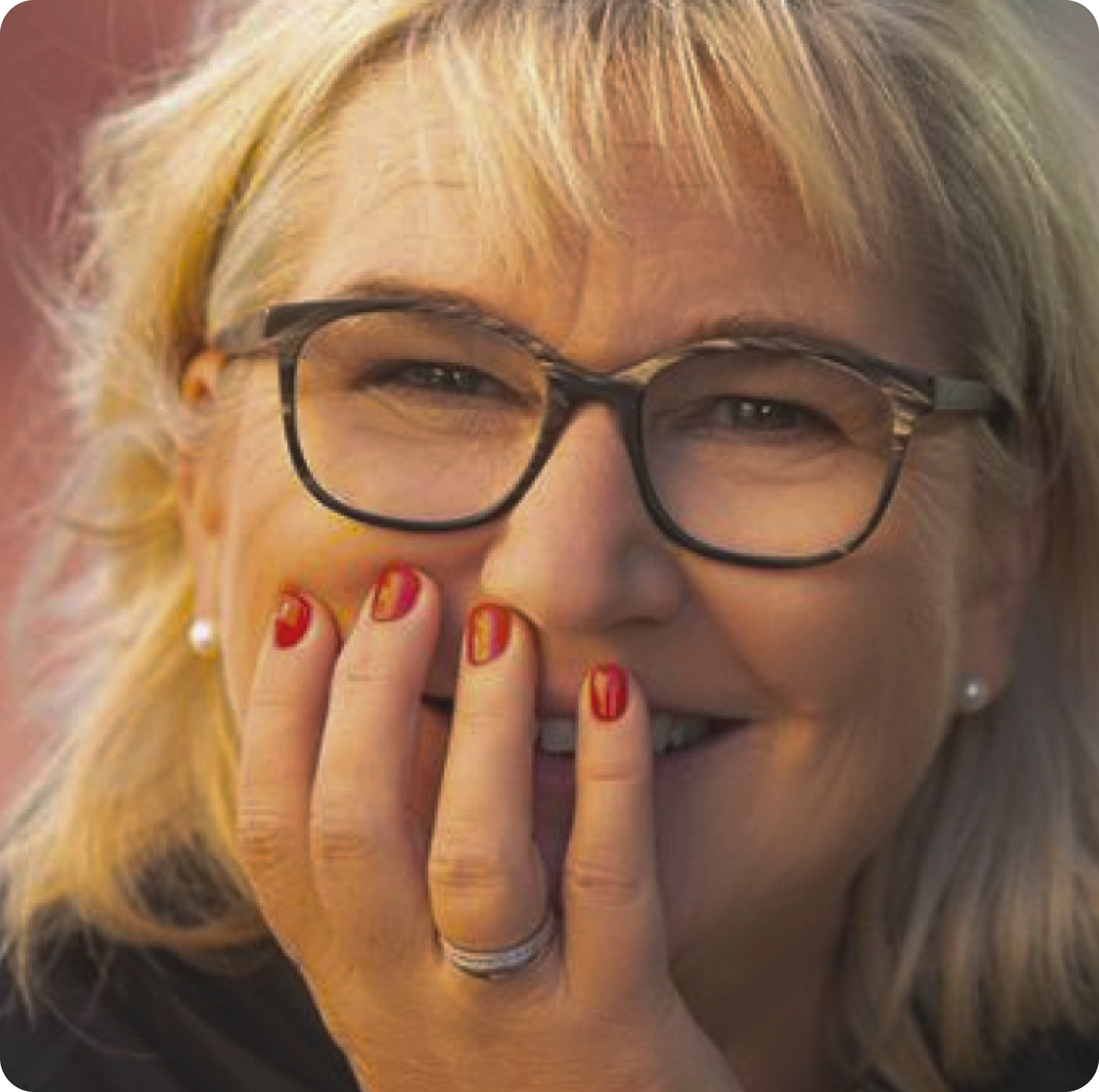 A woman wearing glasses laughs, one hand in front of her face