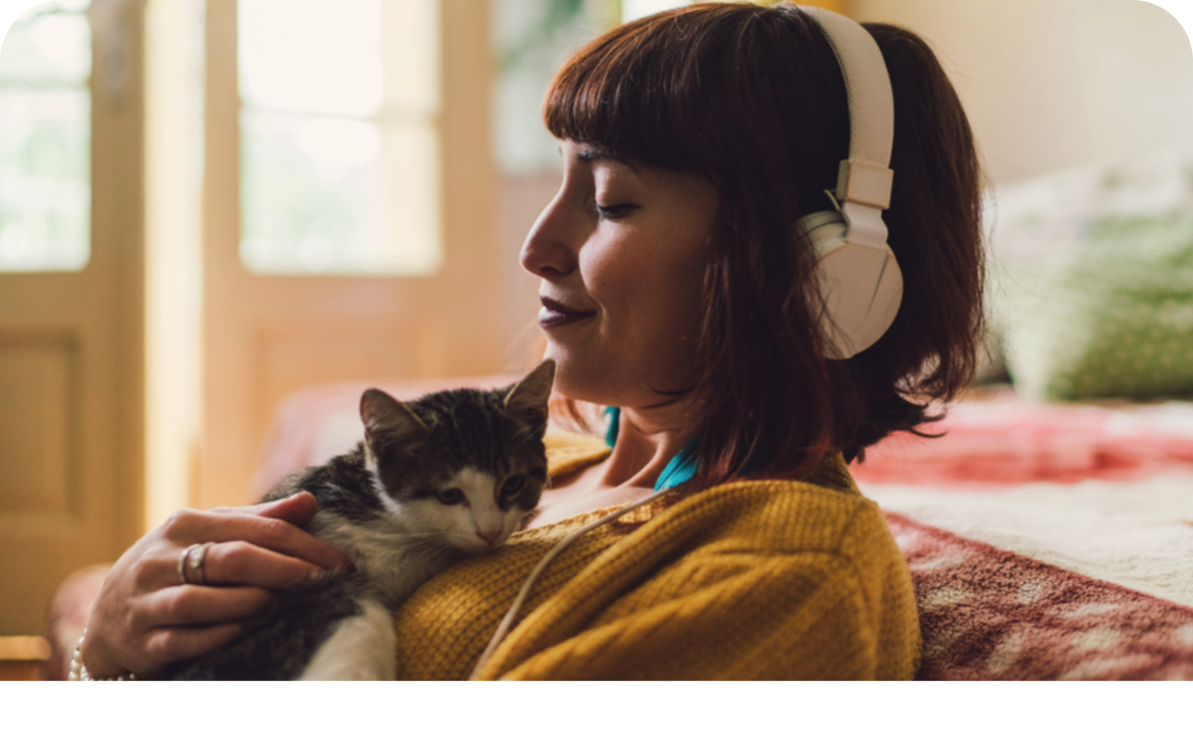 A woman wearing headphones sits relaxed on the sofa with her cat