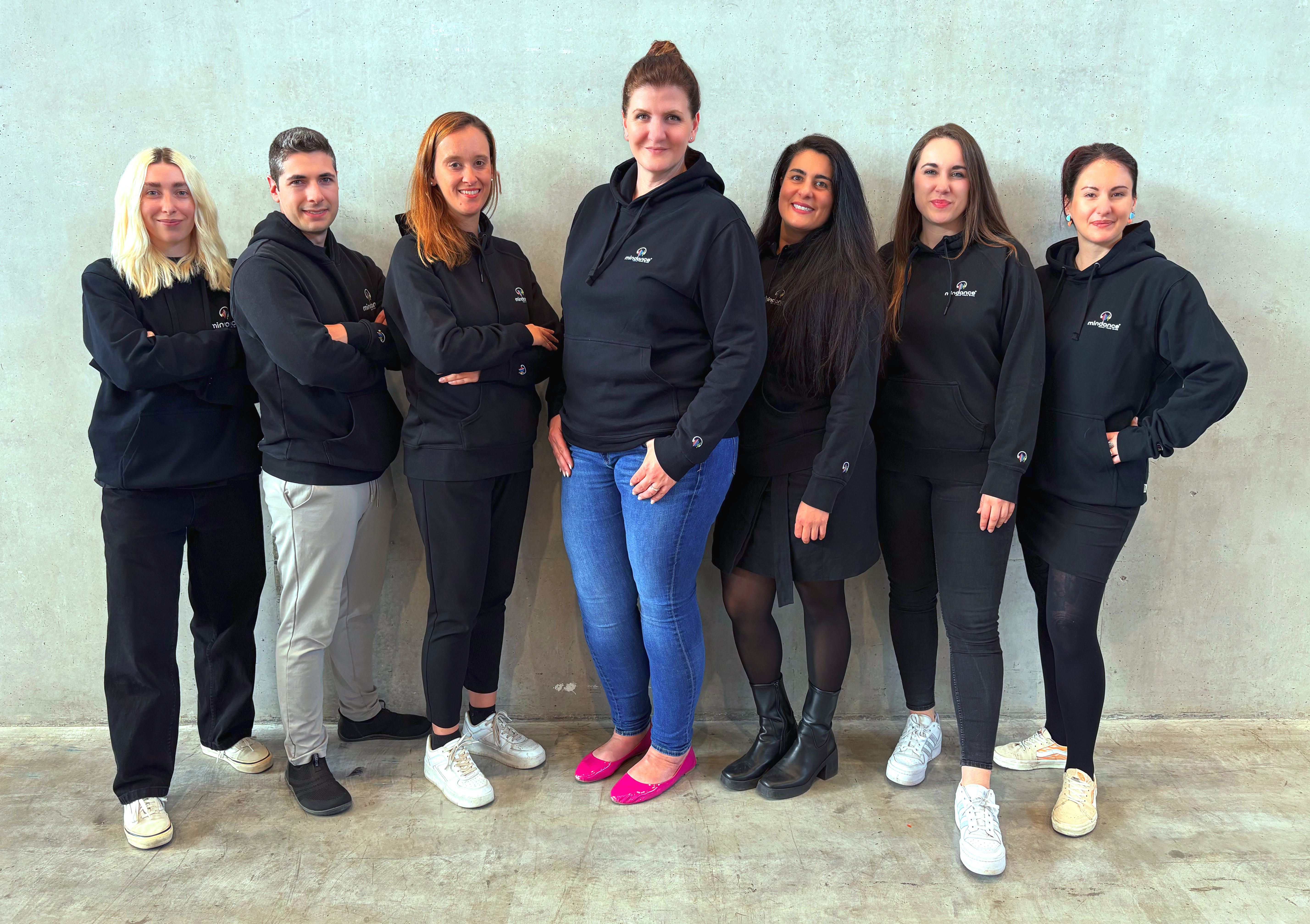 The Mindance team, seven people side by side in front of a light concrete wall