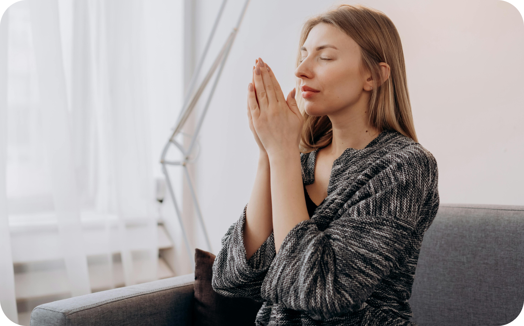 A woman sits on the sofa with her eyes closed and her hands pressed together