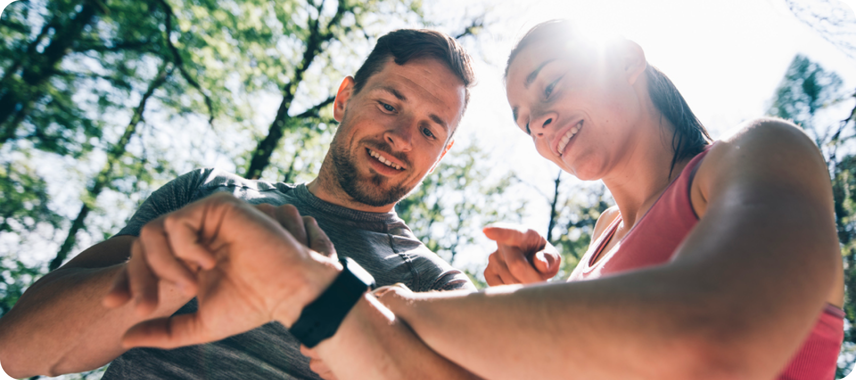 Zwei Sportler:innen im Wald schauen gemeinsam lächelnd auf eine Sportuhr